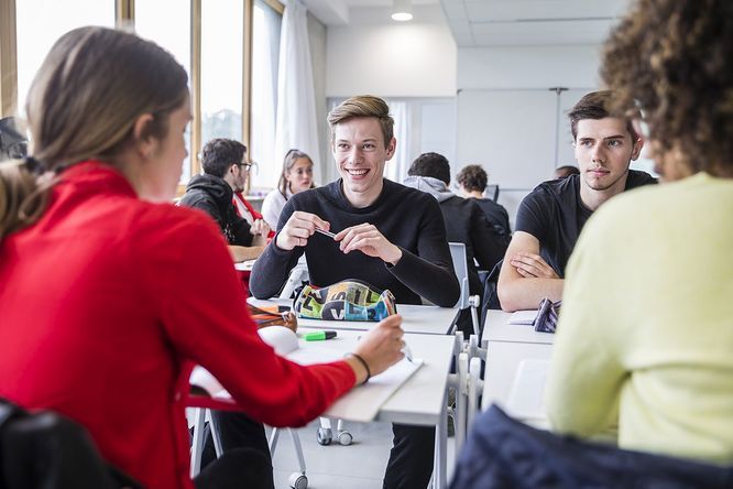 2 Lycéens face à 2 lycéennes de dos, assis autour de tables dans une classes